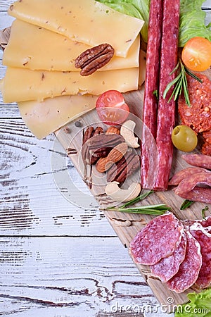 Smoked sausages assortment, cheese, nuts, cherry tomatoes, pickled vegetables and olives on the white wooden table Stock Photo