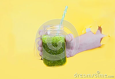 Smoothie from fresh herbs in a glass jar is held by a man`s hand in a hole on a yellow background Stock Photo