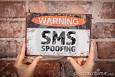 SMS SPOOFING. A woman is holding a warning sign with text. Red brick background Stock Photo