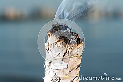 Smudging Ritual using burning thick leafy bundle of White Sage on the beach at sunrise in front of the lake Stock Photo