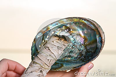 Smudging Ritual using burning thick leafy bundle of White Sage in bright polished Rainbow Abalone Shell on the beach at sunrise Stock Photo