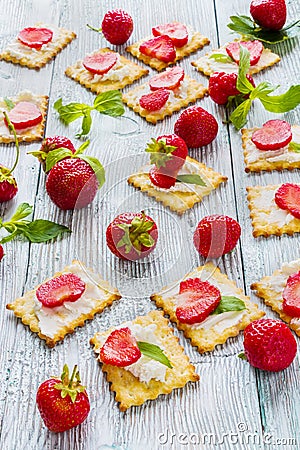 Snack: crackers with cream cheese, fresh strawberries and mint leaves on light wooden background Stock Photo