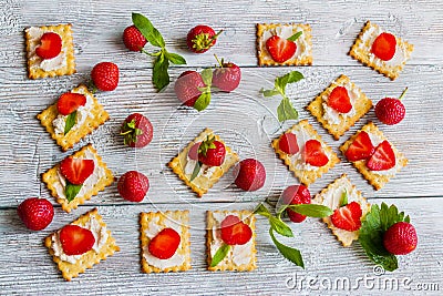 Snack: crackers with cream cheese, fresh strawberries and mint leaves on light wooden background Stock Photo