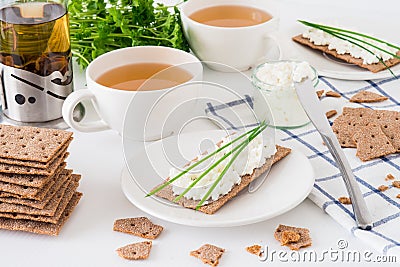 Snack with fresh tea and rye crispy bread Swedish crackers with cottage cheese, decorated with thin green onion, on white backgr Stock Photo