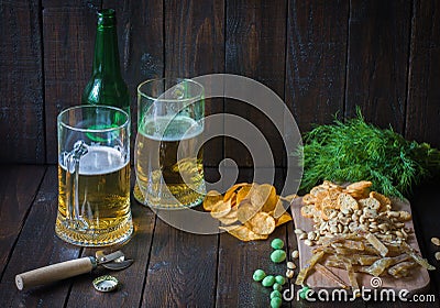 Snacks to beer, on a wooden board and two mugs of beer.Chips, peanuts, pieces of fish,crackers, dill, bottle.Copy space. Stock Photo