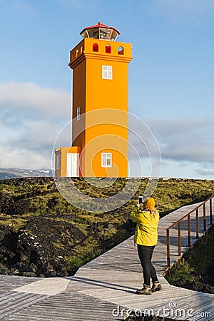 SNAEFELLSNES,Woman in yellow raincoat taking picture of Svortuloft Lighthouse, Snaefellsnes peninsula, Iceland Stock Photo