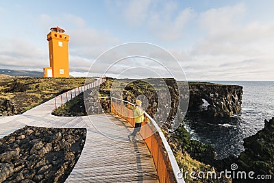 SNAEFELLSNES,Woman in yellow raincoat watching sunset at Svortuloft Lighthouse, Snaefellsnes peninsula, Iceland Stock Photo