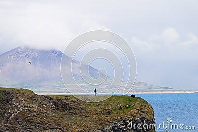 Unidentified tourists standing at the cliff near Gatklettur Stone Arch, Iceland Editorial Stock Photo