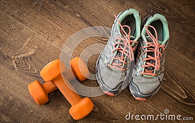 Sneakers and pair of orange dumbbells on wooden background. Weights for a fitness training. Stock Photo