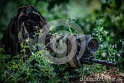 Sniper in camouflage suit in an ambush among the bushes. The shooter aims from a carbine with an optical sight Stock Photo