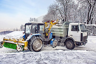 Snow cleaning tractor snow-removal machine loading pile of snow on a dump truck Editorial Stock Photo