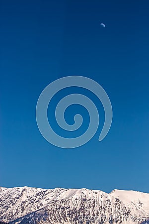 Snow-covered mountain range under a high blue sky and the moon Stock Photo