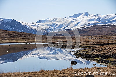 Quiet road runs beside lake reflecting Iceland`s snow covered mo Stock Photo