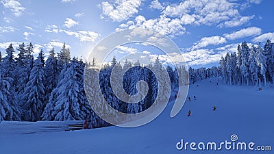 The snow-covered piste for skiers and snowboarders, equipped with snow cannons and safety mesh fencing, runs under a chairlift thr Stock Photo
