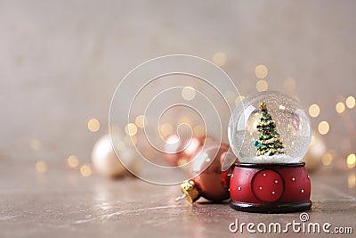 Snow globe with Christmas tree and decorations on marble table against festive lights Stock Photo