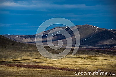 The snow has not yet completely melted on the mountains, clouds float across the sky and form shadow patterns on the mountains Stock Photo