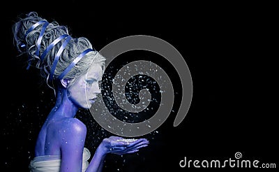 Snow Queen or Winter Witch woman blowing snowflake. Beautiful female model lady with perfect fantasy makeup on black background. Stock Photo