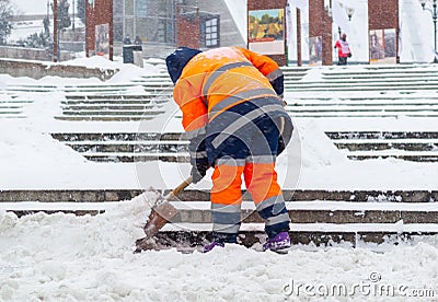 Snow removal in the city. A worker clears snow with a shovel after a snowfall on the steps Stock Photo