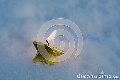 In the snow is a single burning candle in the form of a star. Evening. There is a small light around the candle. New year and Stock Photo