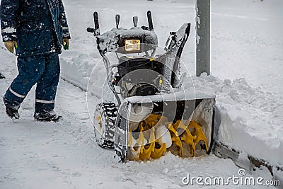 Snowblower parked in the park during a snowfall. Person goes to a snowplow. Stock Photo