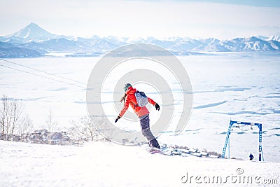 Snowboarder girl in red jacket riding down the hill in front of snowy mountains Stock Photo