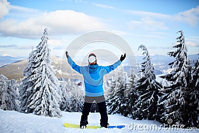 Snowboarder raised his arms and hands to the sky at ski resort. Man climbed a mountain top through forest for Stock Photo