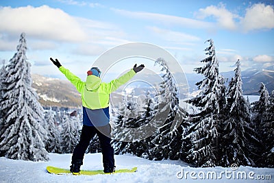 Snowboarder raised his arms and hands to the sky at ski resort. Man climbed a mountain top through forest for Stock Photo