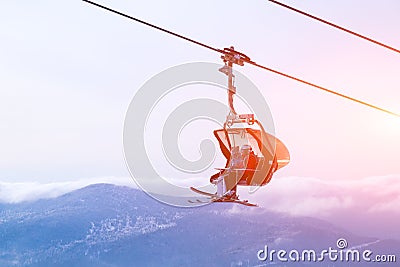 Snowboarder and skier in professional outfit climb up cable car lift up mountains on background of sky, sun and mountain peaks. Editorial Stock Photo