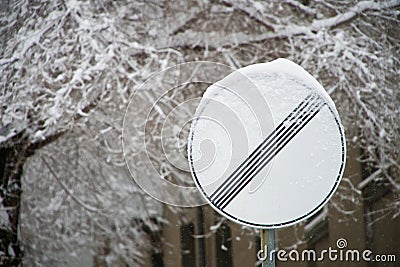 Snowbound road sign: national speed limit applies against a snow-covered tree and an apartment building Stock Photo