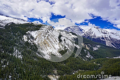 Snow capped Canada`s Rockies mountain during a summer day contrasting with a bright blue sky and white clouds Stock Photo