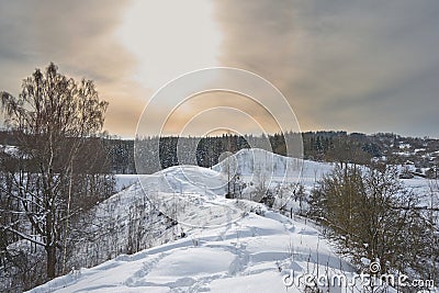 Snowdrifts on winter snow covered small hills, trees and sun shine glow in yellow-blue sky. Stock Photo