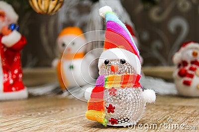 The snowman in a cap and a striped scarf costs on a floor near a fir-tree against the background of other snowmen and Father Frost Stock Photo