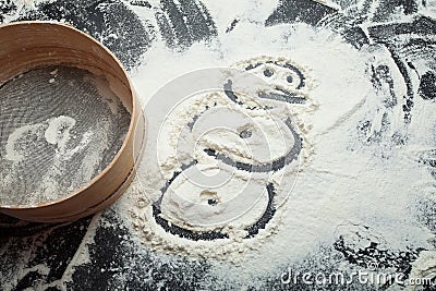 Snowman painted on a flour on a black background. Festive and Christmas baking Stock Photo