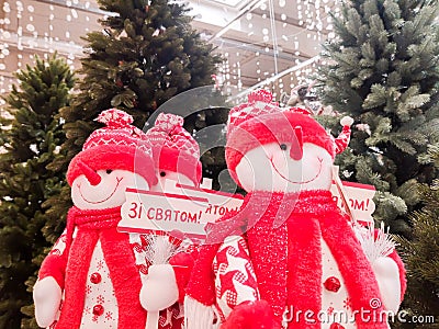 Snowmen are sold on the counters near the Christmas trees in the shopping center, dressed in a red cap and with a sign with Editorial Stock Photo