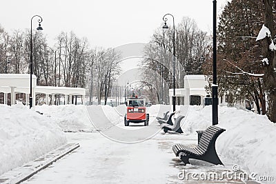 A snowplow removes snow on the road in the park. Stock Photo