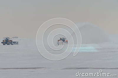 Snowplow removing snow from runways and roads in airport during snow storm, view through window Editorial Stock Photo