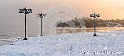 Snowy embankment along the misty river with lanterns at the foggy sunrise - winter landscape. II Stock Photo