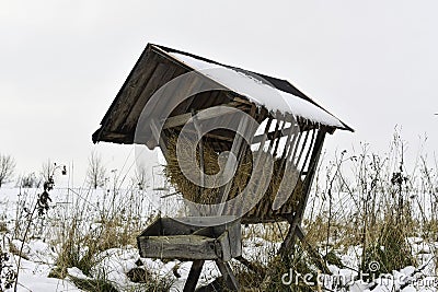 A snowy hay rack in winter. Feeding rack filled with hay and ready for winter feeding of game animals. Concept of the end of the Stock Photo