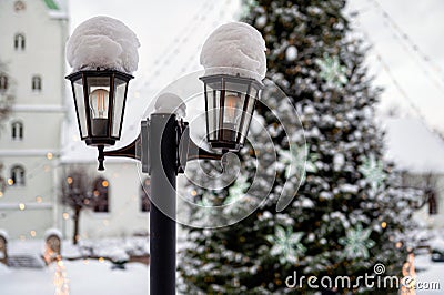 Snowy lantern with decorated Christmas tree and church in blurred background, shallow DOF Stock Photo