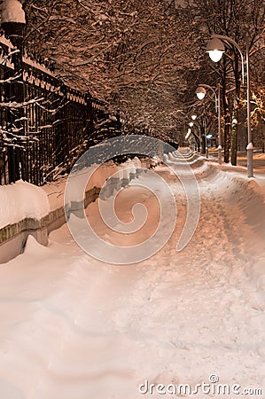 Snowy night pathway in city. Bright light of lanterns. Vertical Stock Photo