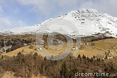 Snowy rocky slopes of Arera peak border green glades with lodges Stock Photo