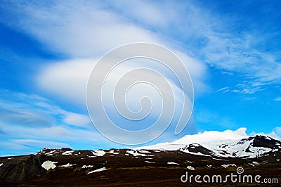 Snowy volcanic mountain and interesting shaped clouds in a sunny day Stock Photo