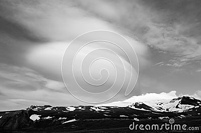 Snowy volcanic mountain and interesting shaped clouds in a sunny day in black and white Stock Photo