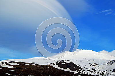 Snowy volcanic mountain in a sunny day and interesting shaped clouds Stock Photo