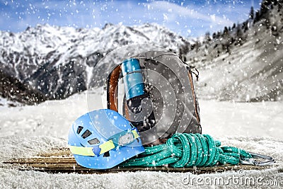 Snowy winter. A wooden board with a grey backpack, a blue helmet and a turquoise rope with blurred mountain background. Stock Photo