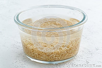 Soaking brown rice cereal in water to ferment cereals and neutralize phytic acid. Large glass bowl with grains flooded with water Stock Photo