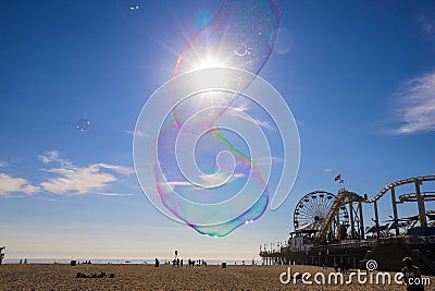 A soap bubble in the sky with people relaxing on the beach and a colorful Ferris wheel and rollercoaster on the pier Editorial Stock Photo