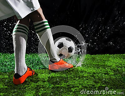 Soccer football players kicking to soccer ball on green grass field with splashing of transparent water against black background Stock Photo