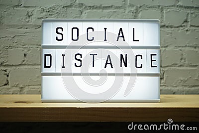 Social Distance word in light box on wooden shelve and white brick wall background Stock Photo