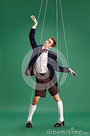 Social manipulation and pressure. Young guy, marionette on string against green studio background Stock Photo